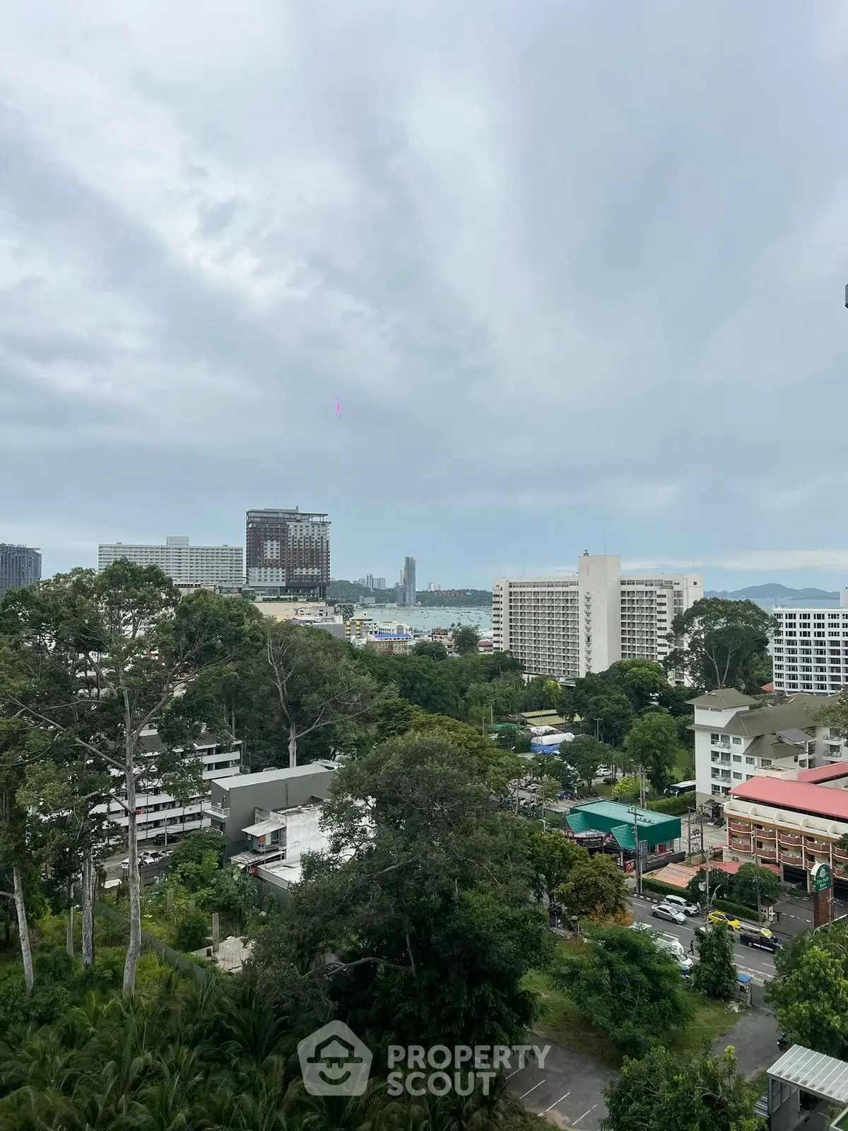 Scenic city view with lush greenery and high-rise buildings under a cloudy sky.
