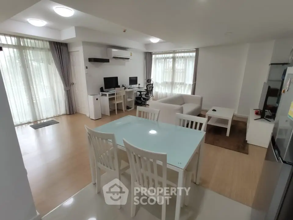 Spacious modern living room with dining area and home office setup, featuring large windows and stylish furniture.