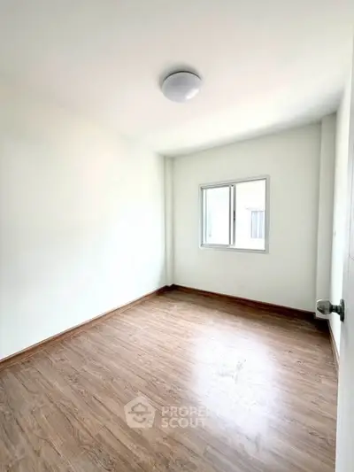 Bright empty room with wooden flooring and a window, perfect for customization.