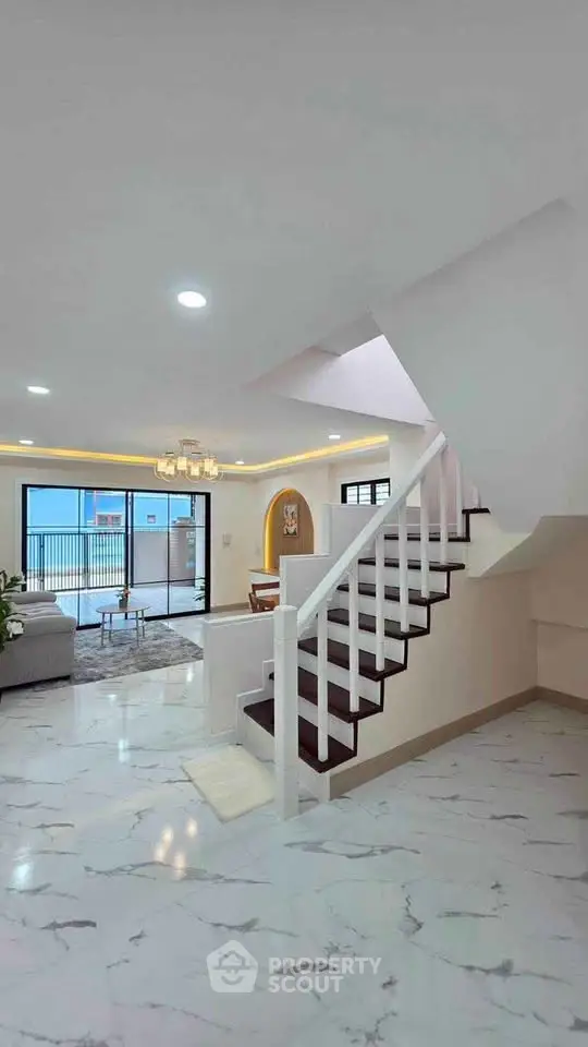 Spacious modern living room with elegant staircase and large windows opening to a balcony.