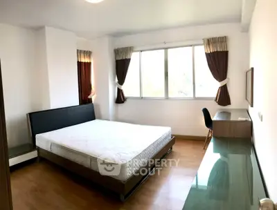 Spacious bedroom with large window and modern furnishings in a well-lit apartment.