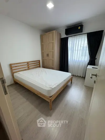 Cozy bedroom with wooden bed frame, wardrobe, and natural light from window.