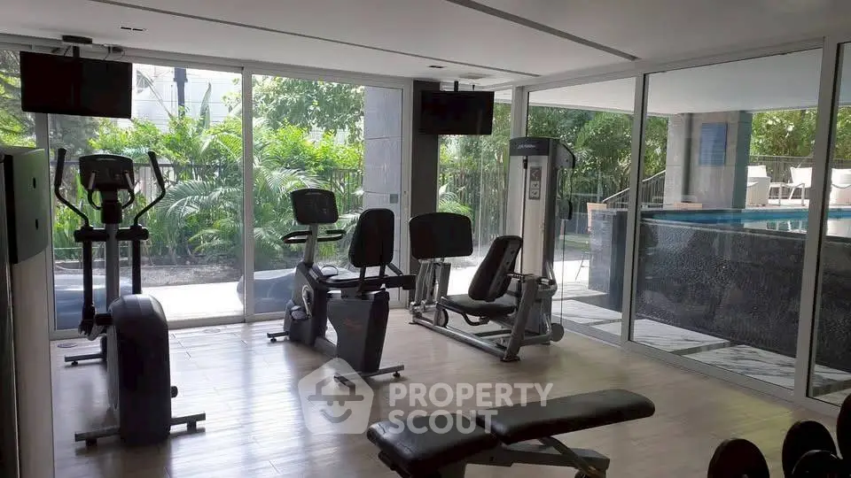 Modern gym with exercise equipment and pool view in luxury apartment complex.