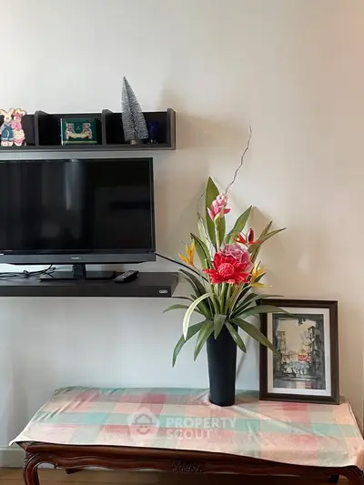 Charming living room corner with TV, elegant shelf, and vibrant floral arrangement on a classic wooden table.