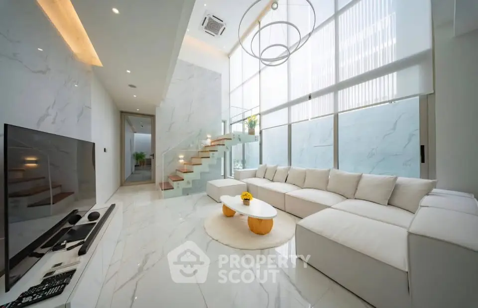 Luxurious modern living room with high ceilings, elegant staircase, and stylish decor.