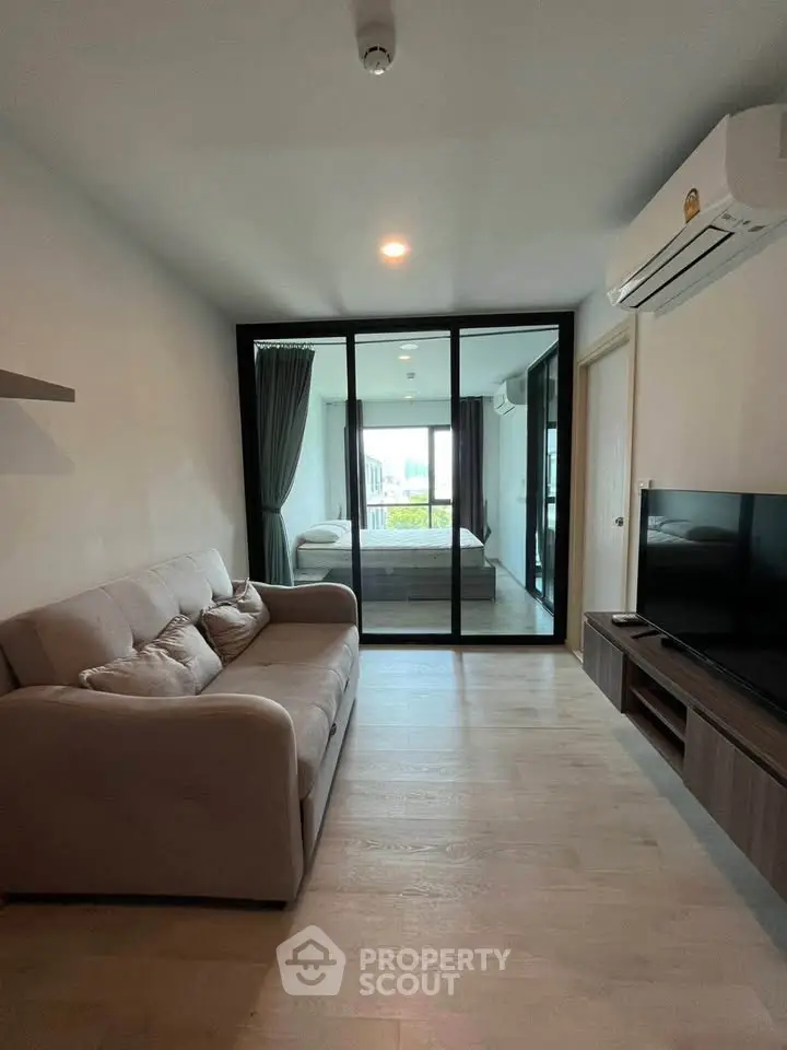 Modern living room with cozy sofa and TV, featuring a glass partition leading to a bedroom.