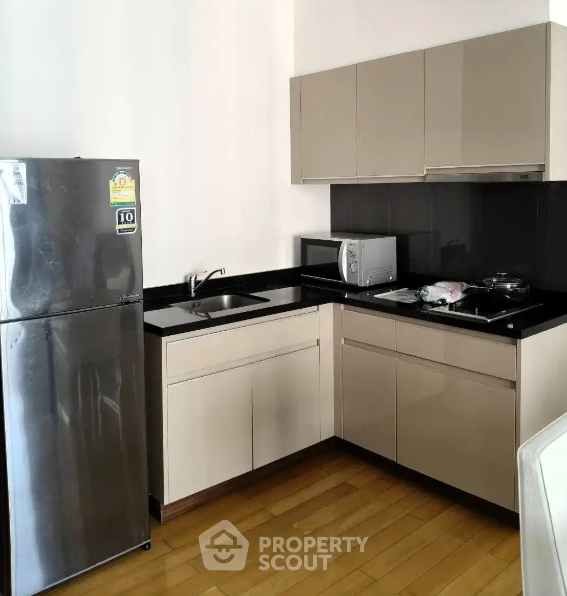 Modern kitchen with sleek cabinets, stainless steel fridge, and wooden flooring in a stylish apartment.