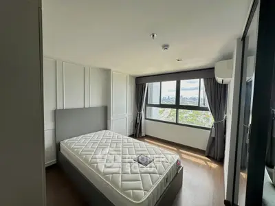 Modern bedroom with large window offering stunning city views, featuring a comfortable bed and sleek design.