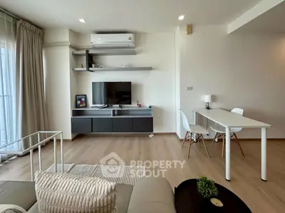 Modern living room with sleek furniture and natural light, featuring a wall-mounted TV and dining area.
