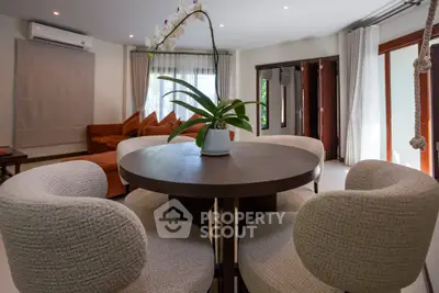 Elegant living room with modern round table and plush chairs, featuring large windows and stylish decor.