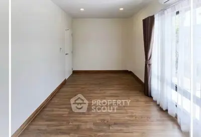 Spacious empty room with wooden flooring and large window, perfect for customization.