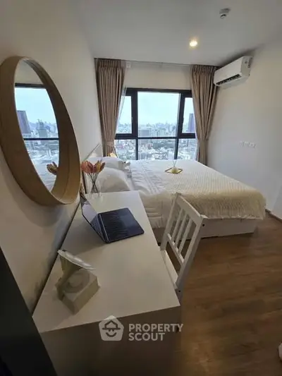 Modern bedroom with city view, featuring a cozy bed, desk, and large window for natural light.