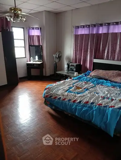 Spacious bedroom with wooden flooring, large bed, and natural light from window.