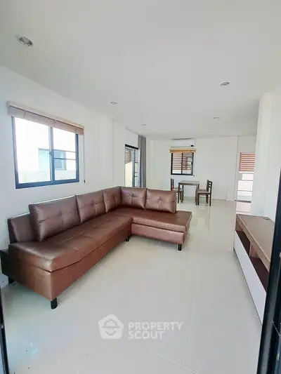 Spacious modern living room with brown leather sectional and dining area, featuring large windows and sleek tile flooring.