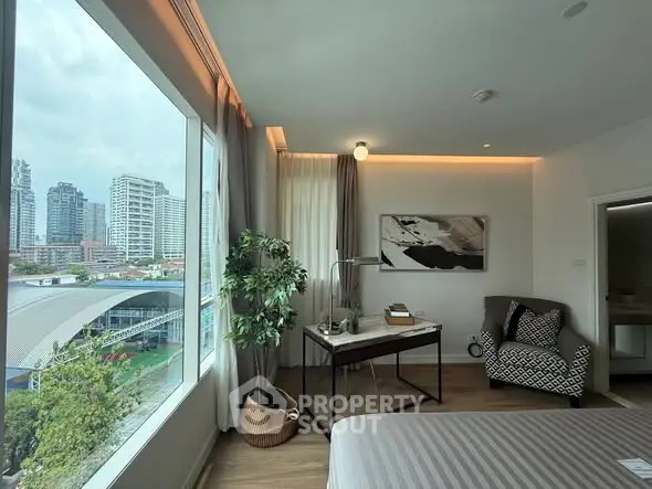 Modern bedroom with large window offering city view, stylish decor, and cozy seating area.