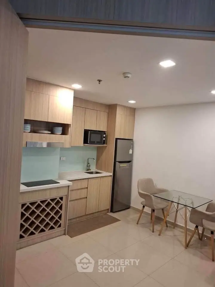 Modern kitchen with sleek cabinetry, glass dining table, and built-in wine rack in a cozy apartment.