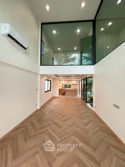 Spacious modern living room with high ceilings and open kitchen layout, featuring elegant wooden flooring and large windows.