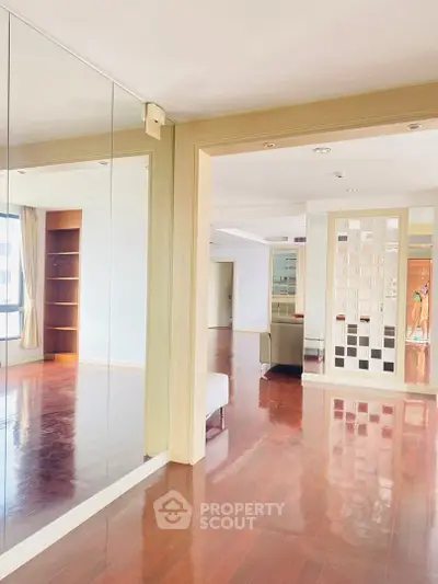 Spacious living room with elegant wooden flooring and mirrored wall in modern apartment.