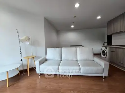 Modern living room with sleek sofa and integrated kitchen featuring washing machine.