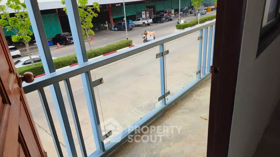 Charming balcony view overlooking a bustling street with greenery and parked cars.