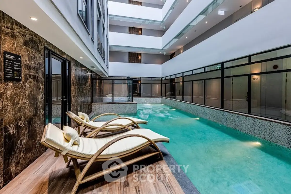 Luxurious indoor pool with elegant lounge chairs in modern apartment complex.
