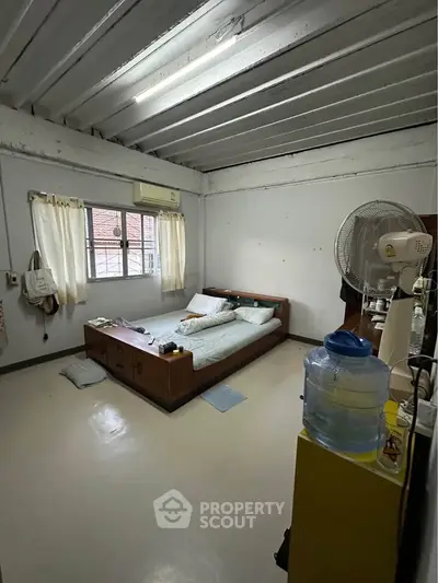 Cozy bedroom with minimalist decor and natural light, featuring a wooden bed and air conditioning.