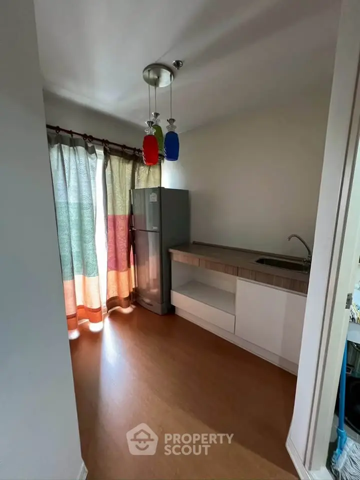 Modern kitchen with sleek cabinetry and colorful pendant lights, featuring a spacious fridge and wooden flooring.