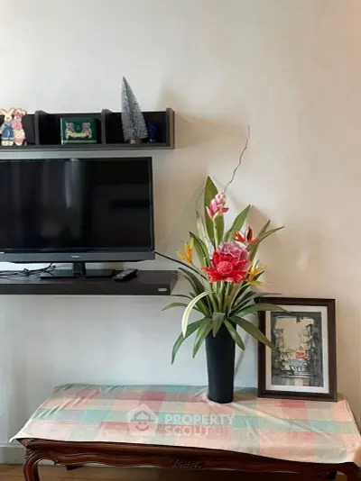 Charming living room corner with TV, decorative shelf, and elegant floral arrangement.