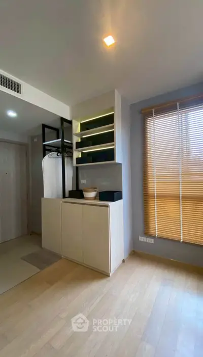 Modern interior with wooden flooring, built-in storage, and large window with blinds.