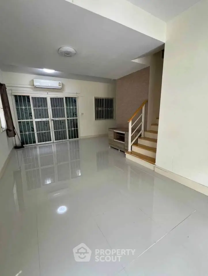 Spacious living room with glossy tiled floors and staircase, featuring large windows and air conditioning.