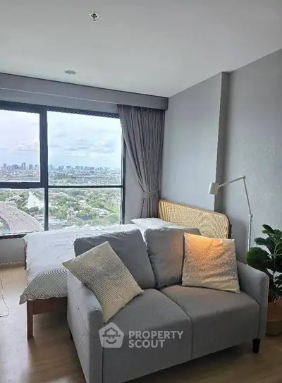 Modern bedroom with city view, cozy sofa, and large window for natural light.