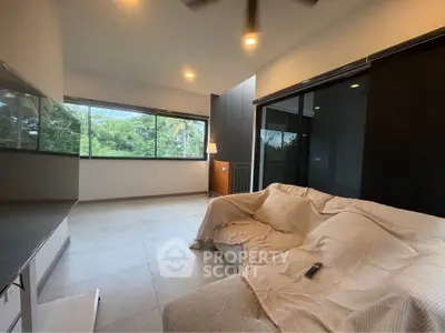 Spacious living room with large windows and modern decor, offering a serene view of lush greenery.