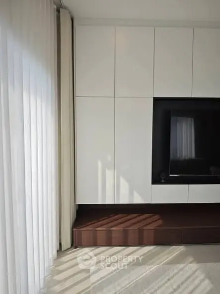 Modern living room with sleek white cabinetry and large window drapes