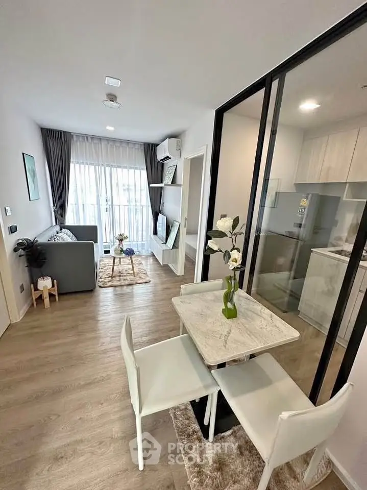 Modern open-plan living room with dining area and kitchen, featuring sleek furniture and large windows.