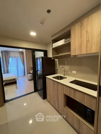 Modern apartment kitchen with sleek cabinetry and open layout leading to a cozy bedroom.