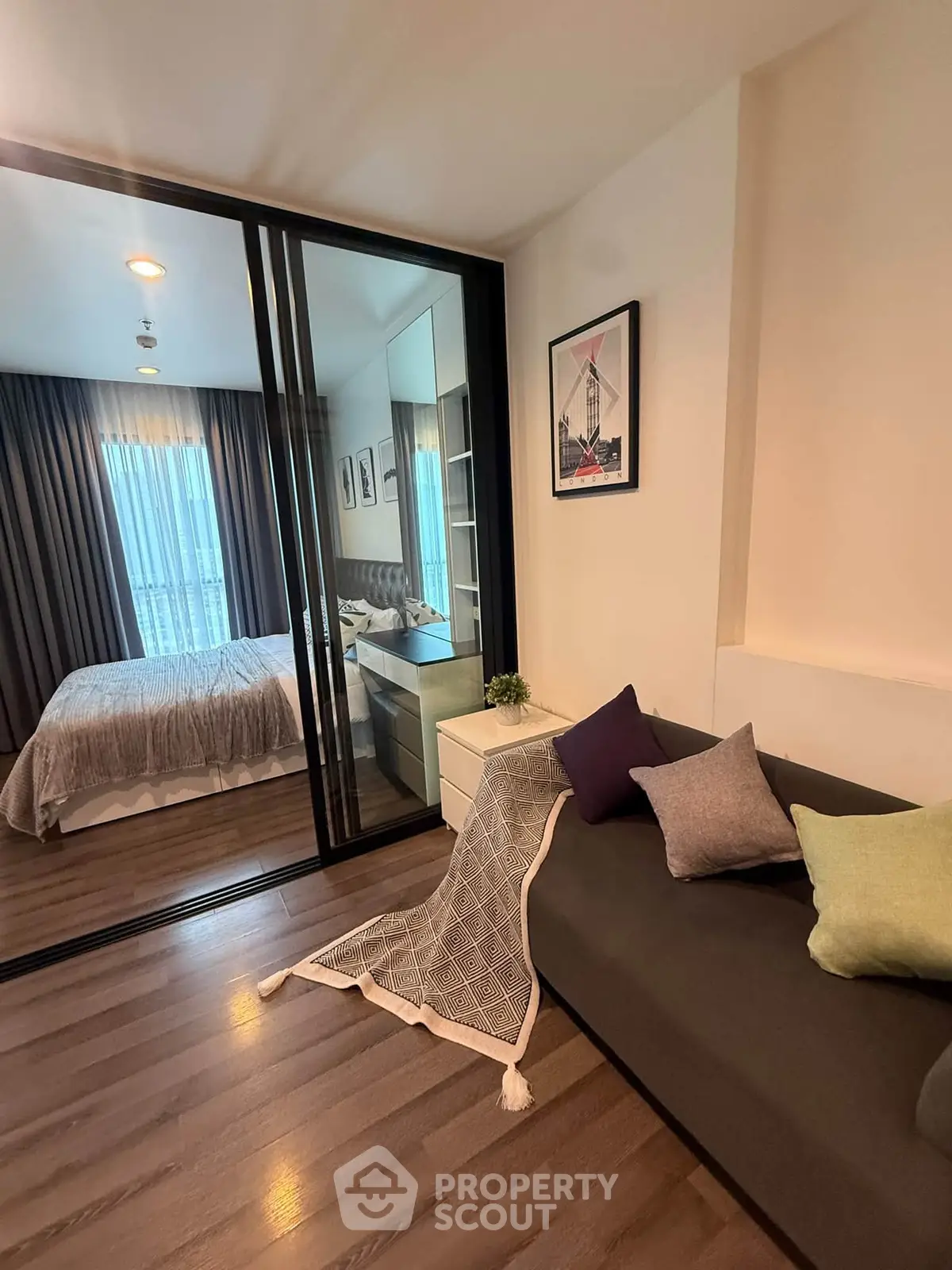 Modern apartment interior with cozy living area and stylish bedroom separated by glass doors.