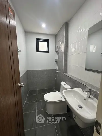 Modern bathroom with sleek design and gray tiles, featuring a shower and white fixtures.
