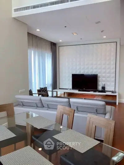 Modern living room with stylish decor and large TV, featuring elegant dining area and natural light.