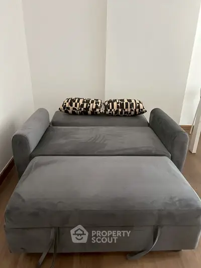 Modern gray sofa bed with patterned cushions in a minimalist living room setting.