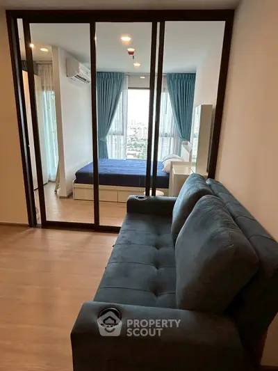 Modern apartment with glass partition separating living room and bedroom, featuring stylish blue sofa and curtains.