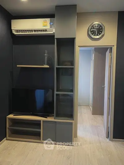 Modern living room with sleek TV unit and air conditioning, featuring stylish decor and open doorway.