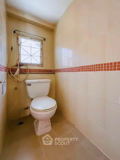 Compact bathroom with tiled walls and window, featuring a toilet and showerhead.