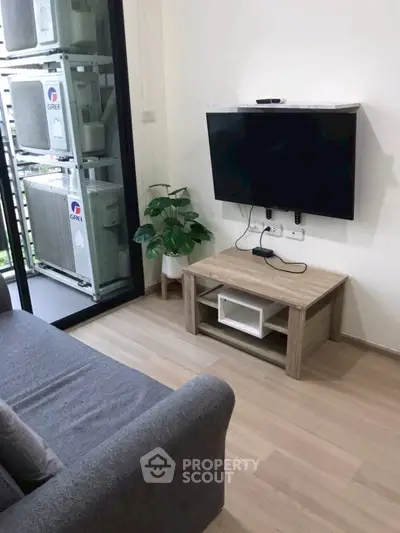 Modern living room with wall-mounted TV and cozy sofa, featuring sleek wooden flooring and a touch of greenery.