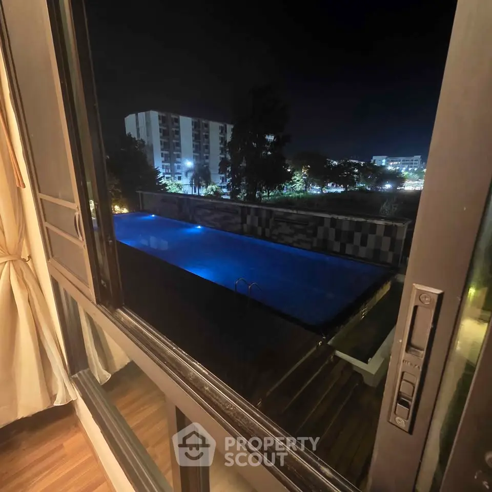 Luxurious night view of illuminated pool from apartment window, showcasing serene urban living.