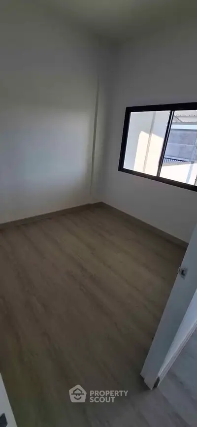 Spacious empty room with large window and wooden flooring, perfect for customization.