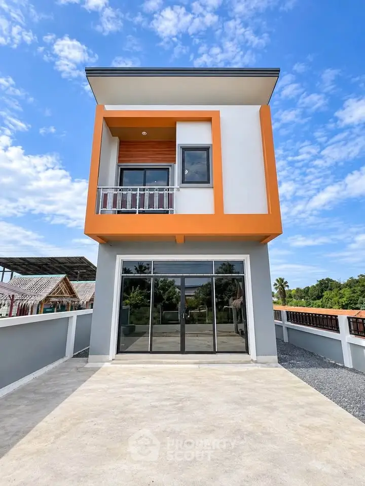 Modern two-story house with vibrant orange accents and large glass doors, set against a clear blue sky.