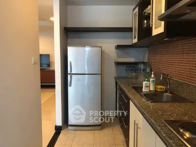Modern kitchen with granite countertops and stainless steel fridge in open layout apartment.