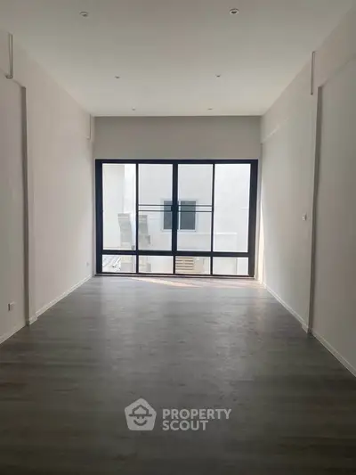 Spacious empty room with large window and modern flooring, perfect for customization.