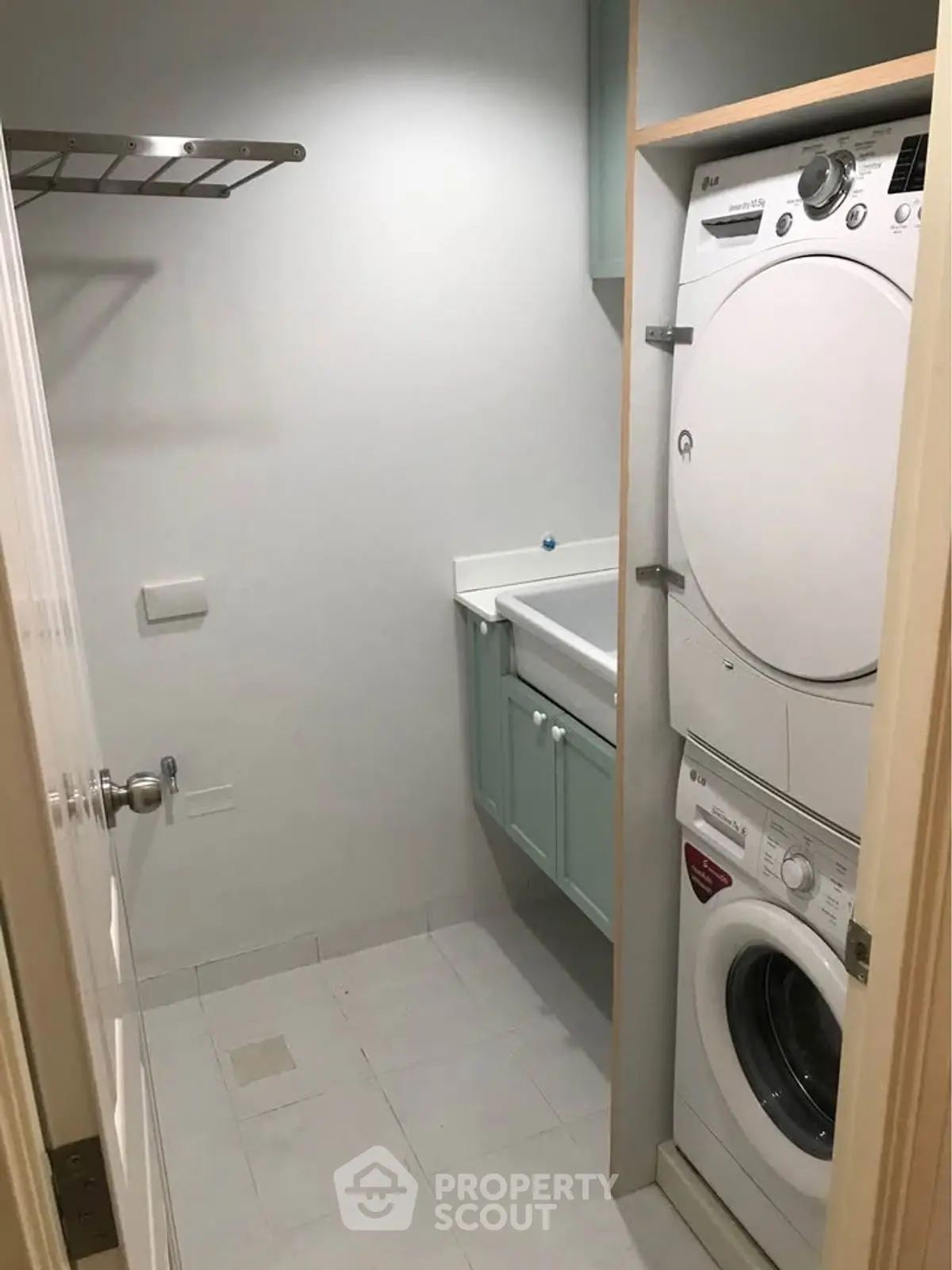 Compact laundry room with stacked washer and dryer, wall-mounted sink, and storage shelf.