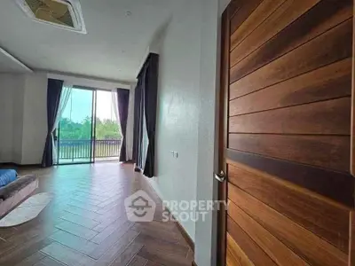 Spacious living room with large windows and balcony access, featuring elegant wooden flooring.
